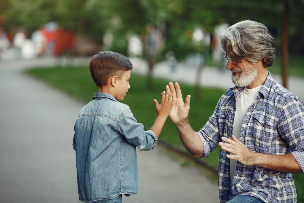 Joyful moment of a grandfather and grandson playing high-five game in the park.