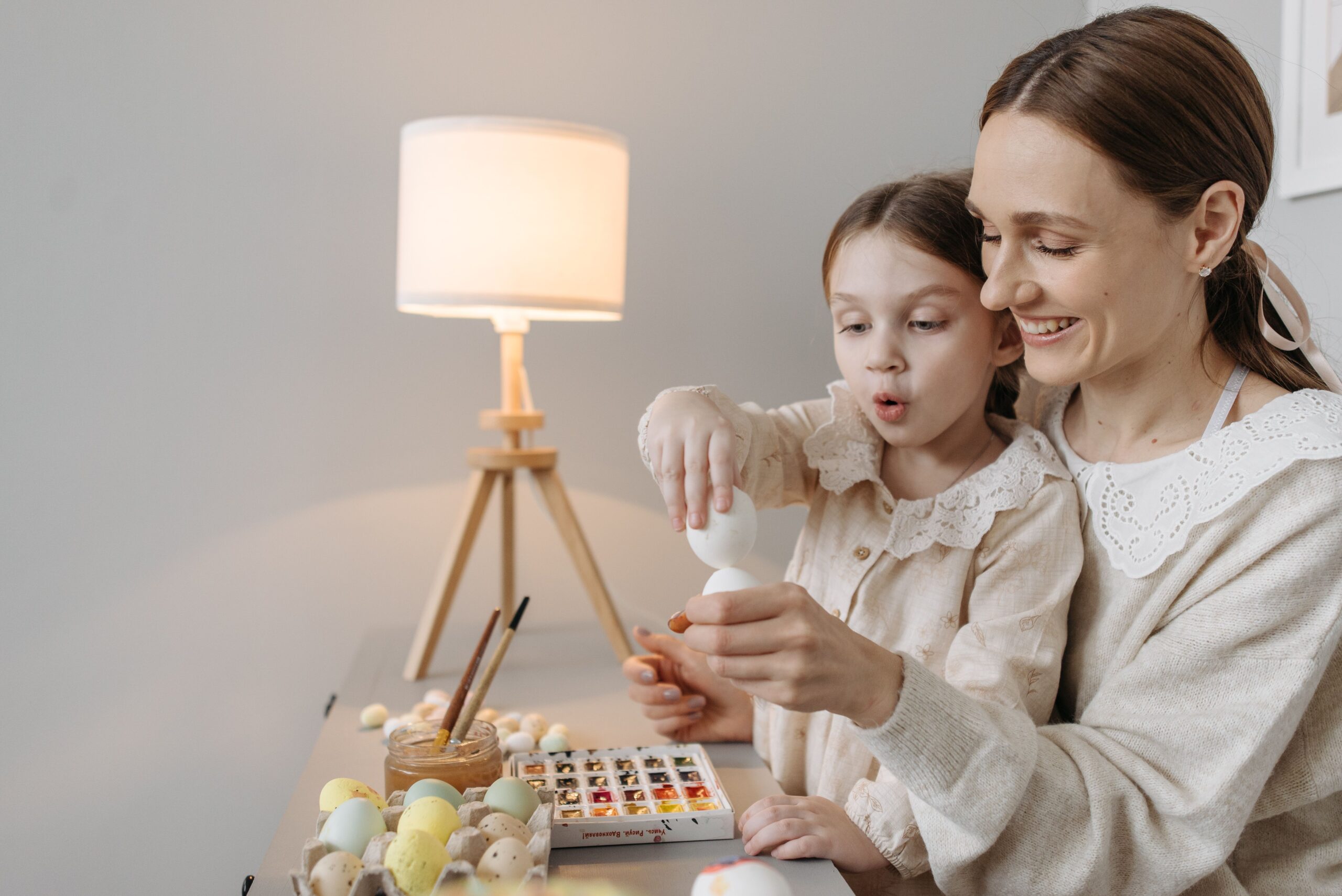A joyful mother and daughter painting Easter eggs indoors, creating a festive atmosphere.